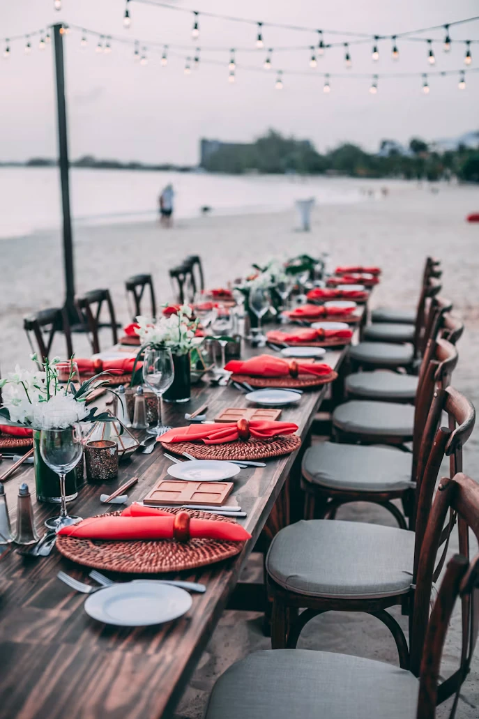 Beachside table setup with red napkins under string lights
